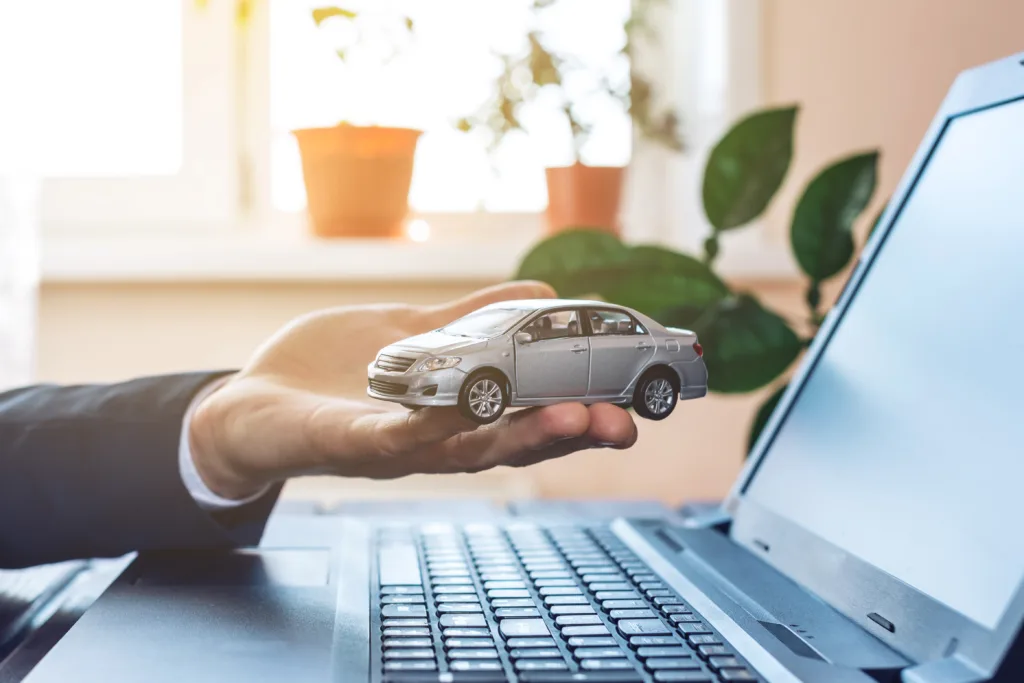 Man in suit working with laptop holding in hand the car. The concept of finding and buying cars on the Internet